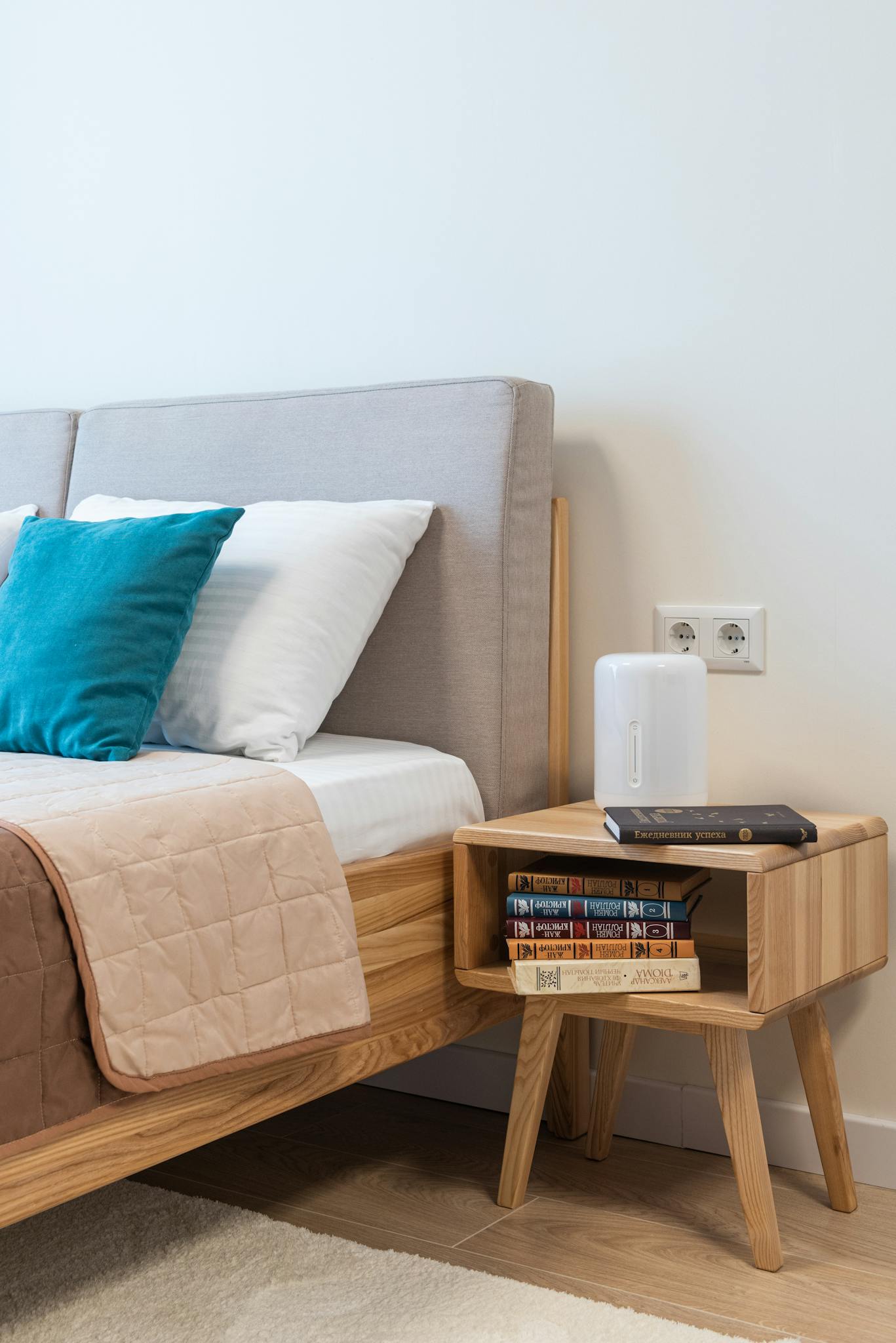 Comfortable bed covered with coverlet with soft pillows near stack of books on wooden bedside table